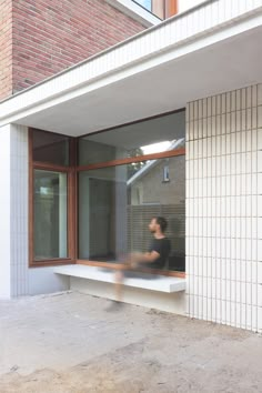 a woman sitting on a window sill in front of a brick building with large windows