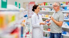 a pharmian talking to a woman in a pharmacy shop with shelves full of medicines