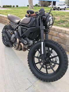 a black motorcycle parked on the side of a road next to a brick wall and grass