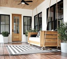 a porch with a swing bed and potted plants on the front porch, next to a door