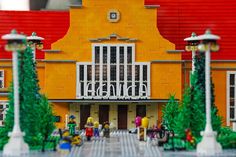 a lego model of a yellow building with trees and people on the front porch in front of it