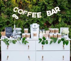 a coffee bar is set up on a dresser with greenery and signs above it