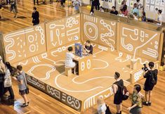 a group of people standing around a display in a room filled with wooden flooring