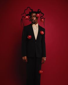 a man in a black suit with red apples on his head, standing against a red background