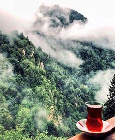 a cup of tea sitting on top of a wooden table next to a mountain covered in clouds