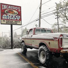 an old red and white truck parked in front of a auto body sign on a snowy day