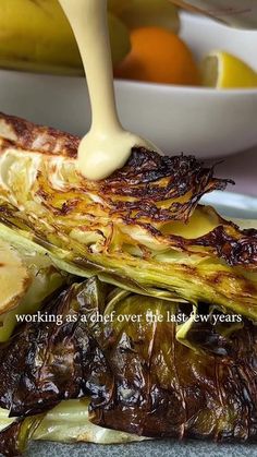 someone is pouring sauce on some artichokes with bananas and oranges in the background