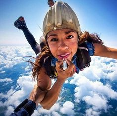 a woman is skydiving over the clouds with her hands on her hips and mouth open