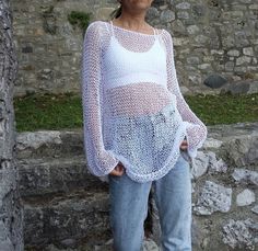 a woman standing next to a stone wall with her hands in her pockets and looking at the camera