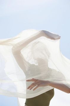 a woman with her hands on her hips under a white sheet flying a butterfly in the sky