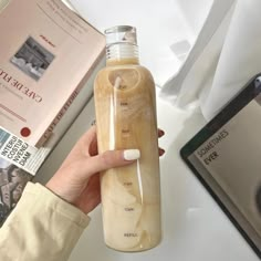 a person holding a glass bottle filled with liquid on top of a table next to books