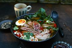 a bowl of soup with meat, noodles and vegetables next to a cup of coffee