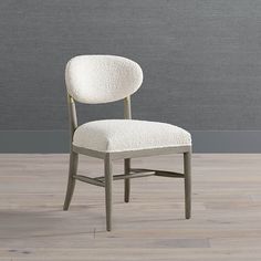 an upholstered chair sits in front of a gray wall and wood flooring