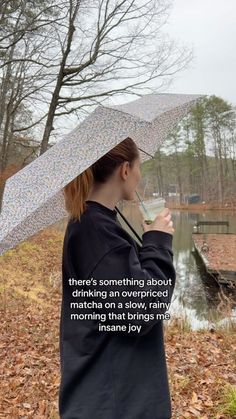 a woman holding an umbrella over her head while standing in the woods with leaves on the ground