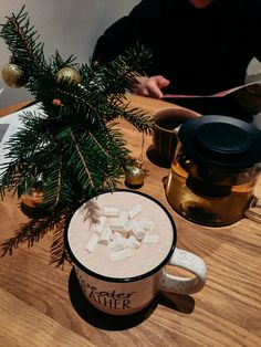 a mug with marshmallows in it sitting on a table next to a potted plant