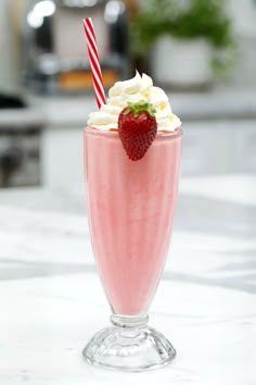 a strawberry milkshake with whipped cream and strawberries on the rim, sitting on a marble countertop