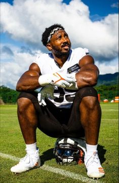 a man sitting on top of a football field wearing a helmet and holding his arms crossed