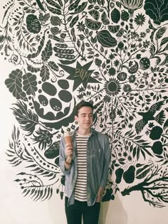 a young man standing in front of a wall with flowers on it and holding an ice cream cone