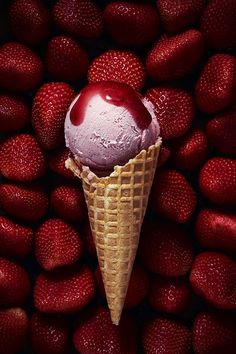 an ice cream cone with a strawberry on top surrounded by strawberries in the background