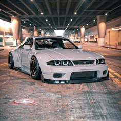 a white sports car parked in an empty parking garage with its hood up and lights on