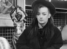 a woman with long hair wearing a hat sitting on a bench in front of a statue