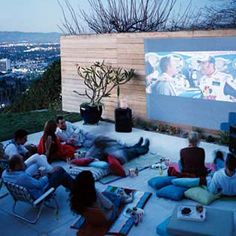 a group of people sitting on the ground in front of a projector screen watching movies