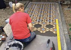 a woman sitting on top of a cement slab next to a tile floor covered in blue and white tiles