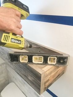 a person using a power drill to fix a piece of wood on top of a toilet