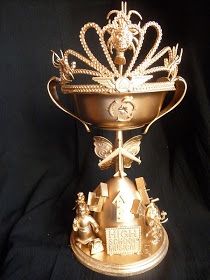 a gold trophy with an ornate crown on it's side and other decorations around the edges