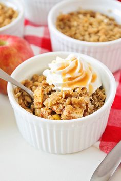 three white bowls filled with oatmeal and topped with whipped cream next to an apple