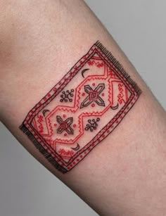 a red and black tattoo design on the left arm, with an intricate border around it