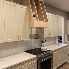 a kitchen with white cabinets and marble counter tops, an oven hood over the stove