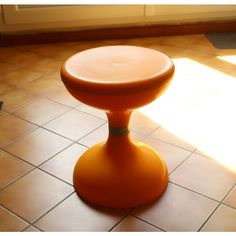 an orange stool sitting on top of a tiled floor