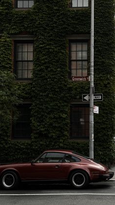 a red car parked on the side of a road next to a tall building covered in ivy