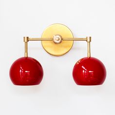 two red balls are hanging from a gold plated wall light, which is mounted on a white wall