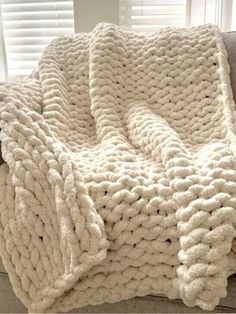 a white knitted blanket sitting on top of a couch next to a windowsill