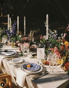 the table is set with flowers and candles for an outdoor dinner party or gathering in the garden