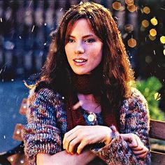 a woman sitting on top of a wooden bench in front of a tree filled with lights