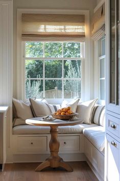 a breakfast nook in the corner of a kitchen with white cabinets and pillows on it