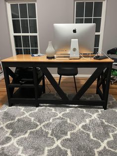 an apple computer sitting on top of a wooden desk in front of two large windows