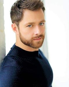 a close up of a person with a beard and wearing a black shirt looking at the camera