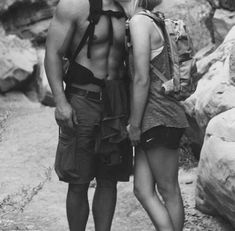 a man and woman standing next to each other in front of some rocks with backpacks on