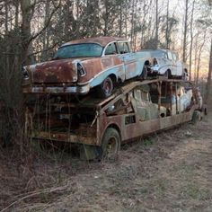 an old rusty car sitting on top of a truck in the woods