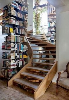 there are many books on the shelves next to the stairs in this room and one chair is up