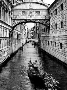 black and white photograph of a boat in the water under an overhanging bridge