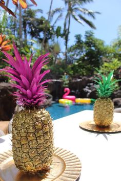 two pineapples sitting on plates near a pool