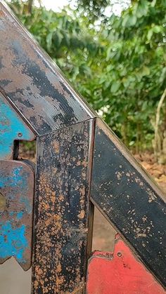 an old metal structure with blue and red paint on it's sides in front of some trees