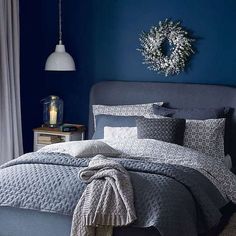 a bedroom with blue walls and grey bedding, wreath on the wall above the bed