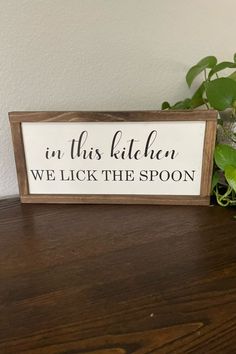 a wooden sign that says in this kitchen we lick the spoon on top of a table