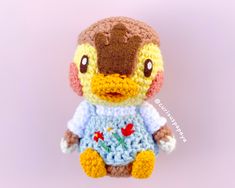 a crocheted stuffed duck wearing a blue and white shirt with flowers on it's chest